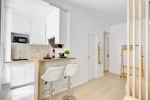 une cuisine avec des placards blancs et deux tabourets blancs dans l'établissement Suite Maxime Chauchat - Paris Opéra, à Paris