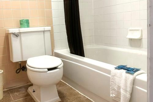 a bathroom with a white toilet and a bath tub at OYO Hickory House Inn in Dexter