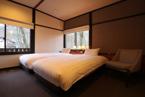 a bedroom with a large bed with a chair and two windows at Hakuba Skala Inn in Hakuba