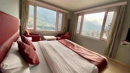 a bedroom with a bed and windows with a view at Hotel Ocean & Hotel Meadows Hill ! Rooftop Restaurant ! Near Hadimba Temple in Manāli