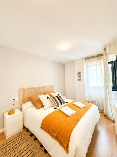 a white bedroom with a large bed with an orange blanket at Apartamento Máis by ALÔGA in Fisterra