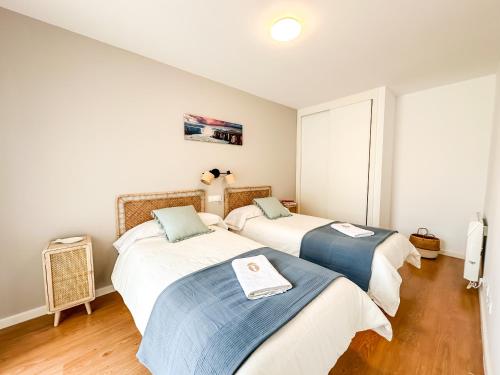 フィステーラにあるApartamento Máis by ALÔGAの白い壁とウッドフロアの客室で、ベッド2台が備わります。