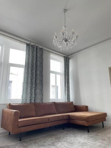 a living room with a brown couch in front of two windows at Pasta apartment Self-Check-in in Liepāja
