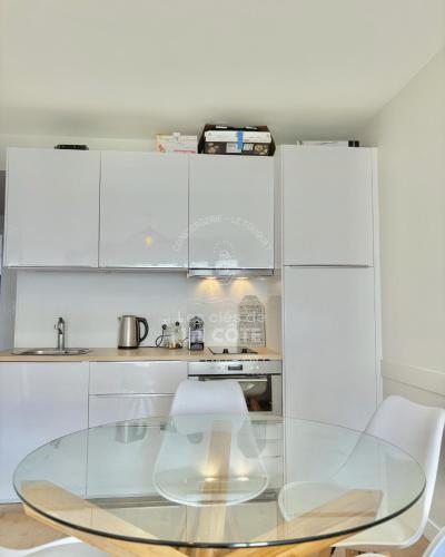 une cuisine avec une table en verre et des placards blancs dans l'établissement Le Bedford, à Le Touquet-Paris-Plage