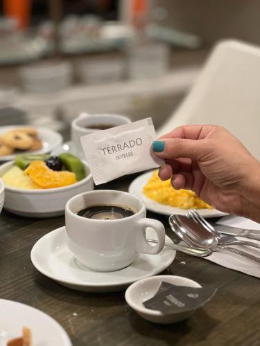 a person holding a piece of paper next to a cup of coffee at Hotel Terrado Providencia in Santiago