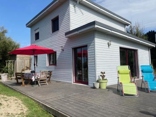 une maison avec une terrasse dotée de chaises et d'un parasol dans l'établissement La cabane de la baie, à Plounévez-Lochrist