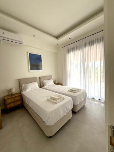 two beds in a white room with two windows at Proti Mare Villa by Toffee Homes in Marathopoli