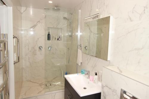 a white bathroom with a shower and a sink at Whale Cove in Whangaparaoa