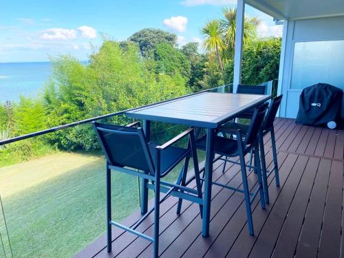 a blue table and chairs on a balcony with the ocean at Whale Cove in Whangaparaoa