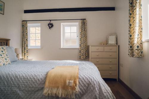 a bedroom with a bed and a dresser and two windows at Cosy Underfloor Heated 17th Century Renovated Mill with Stunning Views - Ty Felin in Beddgelert