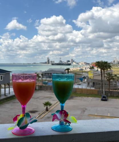 two colorful glasses sitting on a ledge with a view at Corpus Christi North Beach Cozy Condo, 2 Heated pools and Balcony Ocean Views! in Corpus Christi