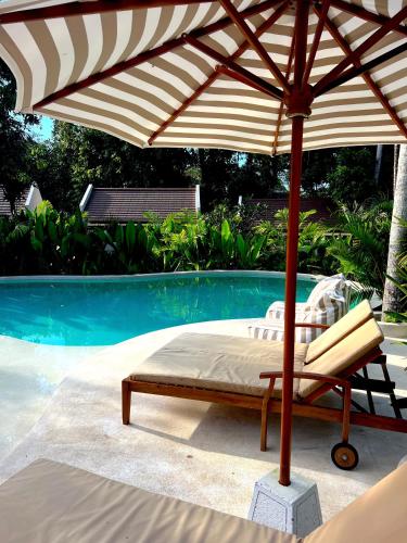 a bed under an umbrella next to a swimming pool at Loku Kedungu - Boutique Resort in Tanah Lot