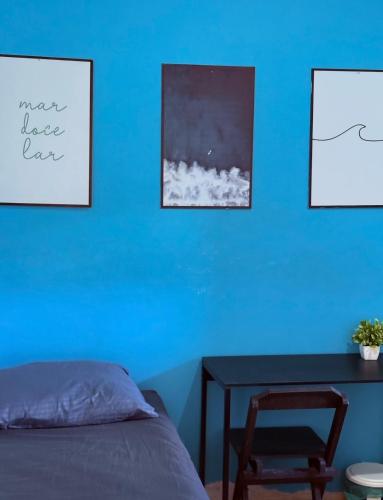 a bedroom with a blue wall with a table and a chair at Pousada Lemon Suítes - Praia do Sesc Acesso Vista Linda e Centro in Bertioga