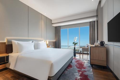 a bedroom with a large white bed and a large window at Grand Mercure Batam Centre in Batam Center