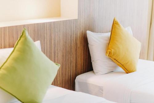 two beds with yellow and white pillows in a room at Aramis Hotel in Nakhon Sawan