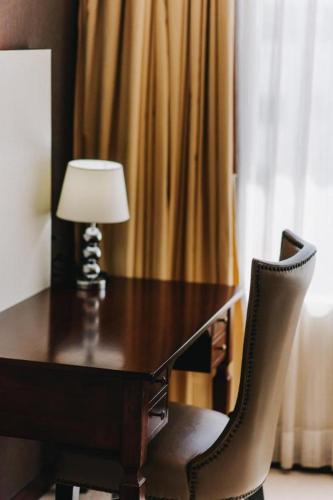 a desk with a lamp and a chair next to a window at Aramis Hotel in Nakhon Sawan
