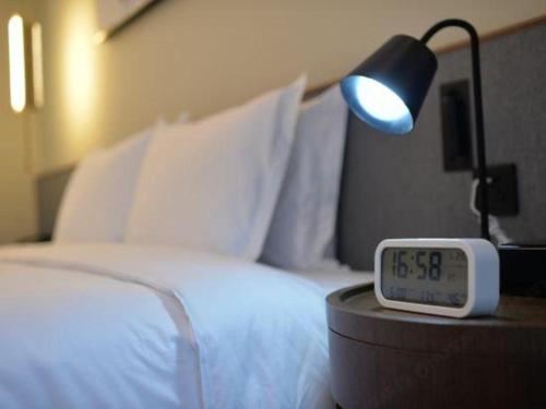 a bed with a lamp and a clock next to it at AURAYA BY SUNING NANJING XUZHUANG in Nanjing