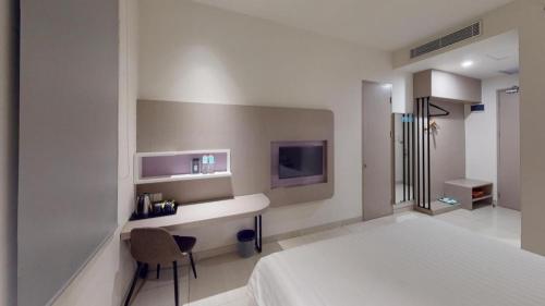 a bedroom with a bed and a desk and a tv at Zoom Dharmahusada Hotel in Surabaya