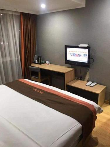a bedroom with a bed and a desk with a television at Jun Hotel Jiangsu Nanjing Gulou District Gupinggang in Nanjing