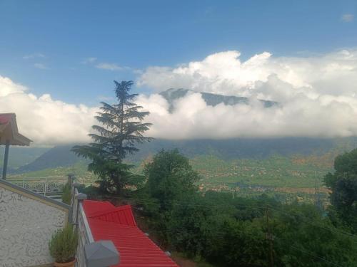 a view of a mountain with a tree and clouds at Anand Vardhan Resorts in Manāli