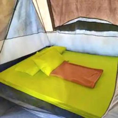a bed with yellow sheets and pillows in a tent at Herman Lantang Camp in Bogor