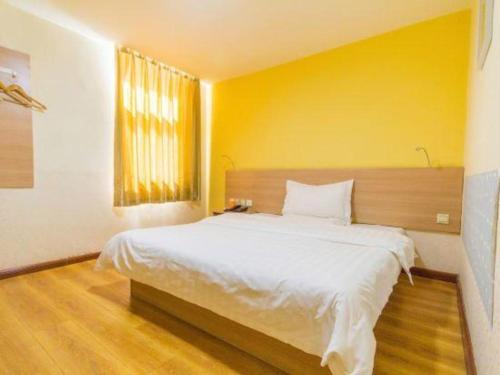 a bedroom with a large white bed with a yellow wall at 7 Days Inn Hohhot University East Street in Hohhot