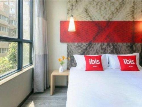 a bed with red pillows in a room with a window at ibis xian North Second Ring Weiyang Rd Hotel in Xi'an
