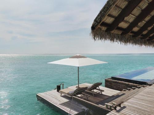 a couple of chairs and an umbrella on the water at One&Only Reethi Rah in Reethi Rah