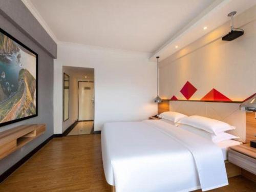 a bedroom with a white bed and a painting on the wall at Borrman Hotel Zhuhai Gongbei Port Fuhuali Light Rail in Zhuhai