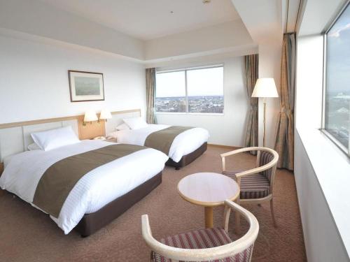 a hotel room with two beds and a table and a window at Grand Hotel New Oji in Tomakomai