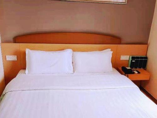 a bed with white sheets and a wooden head board at 7 Days Inn Changchun Zhengyang Street Changchun Park Branch in Changchun