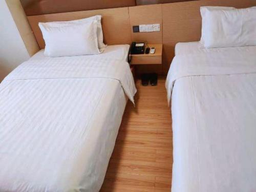 two beds in a hotel room with white sheets at 7 Days Inn Changchun Zhengyang Street Changchun Park Branch in Changchun