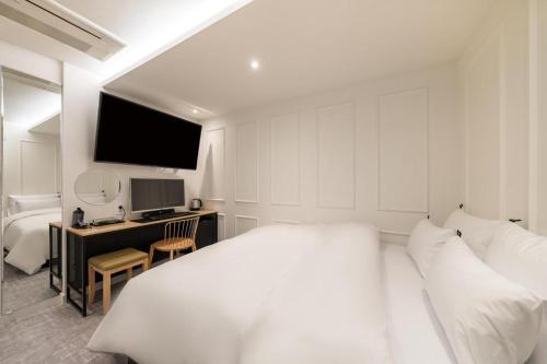 a white bedroom with a bed and a desk with a computer at Crossing Hotel in Seoul