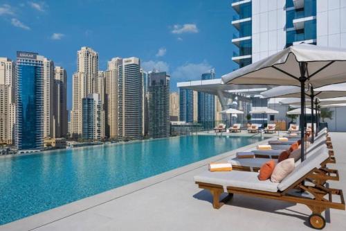 a pool with chairs and umbrellas on a building at Panoramic Marina 1BR City Skyline Views with Balcony, Pool & Gym Access in Dubai