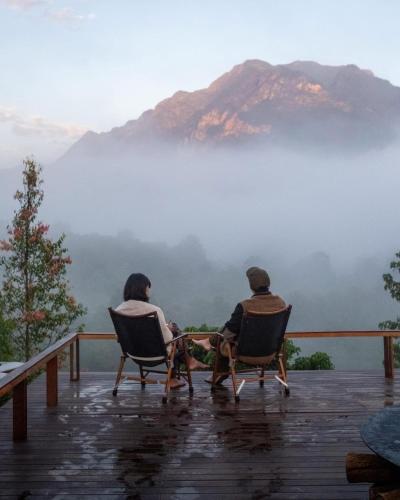 two people sitting in chairs on a deck looking at a mountain at Ruedufon- Private Nature Retreat in Chiang Dao in Ban Tham