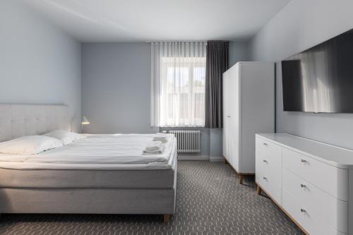 a white bedroom with a bed and a dresser at Roze Park Rooms in Liepāja