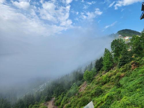 a misty mountain with a road and trees at The Kufri House in Fagu