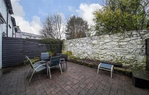 a patio with chairs and tables and a stone wall at Cosy Ramelton Cottage in Ramelton