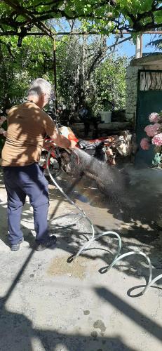 a man is washing a motorcycle with a hose at The Fir Gate in Gjirokastër