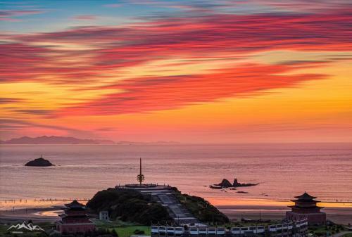 a sunset over a beach with a building and the ocean at Daishan Mountain and Sea Cloud Homestay Sunrise Seaview Bed and Breakfast in Zhoushan