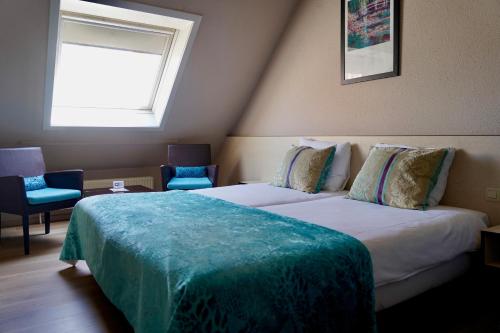 a bedroom with a bed and two chairs and a window at Hotel Prins Boudewijn in Knokke-Heist