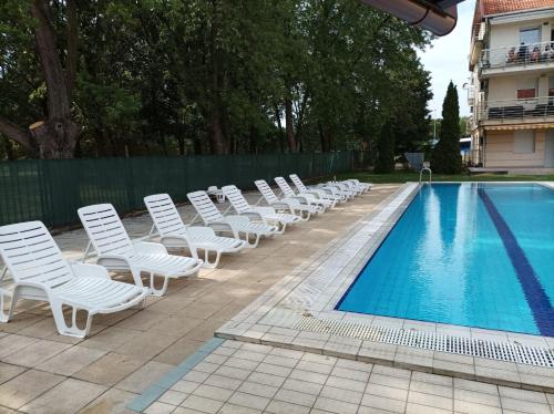 a row of white chairs next to a swimming pool at Casablanca Apartman in Hajdúszoboszló