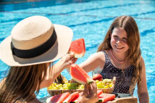 two women sitting in a pool eating fruit at איילת השחר אירוח גלילי - Ayelet Hotel in Ayelet HaShahar