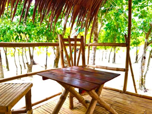a wooden table and bench on a porch with trees at Dosplaya Ecocamp in El Nido