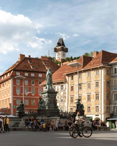a person riding a bike in front of a building with a clock tower at Limehome Graz Trauttmansdorffgasse in Graz