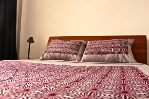 a bed with a red and white comforter and two pillows at B & B Le Nomade in Ouagadougou