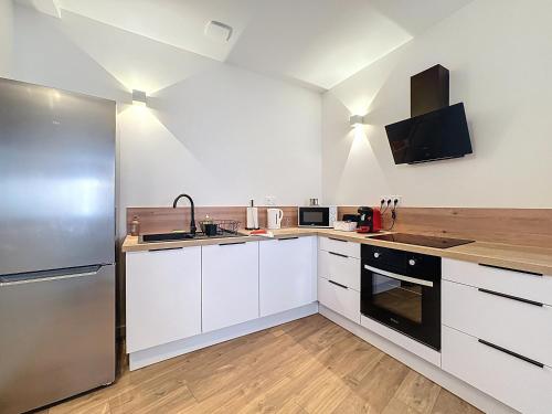 une cuisine avec des armoires blanches et un réfrigérateur en acier inoxydable dans l'établissement Mcosy2, T3, Clim, 6 Personnes, proche A75, à Coudes