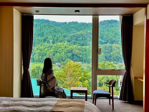 a woman sitting in a chair looking out of a window at 神通峡春日温泉ゆーとりあ越中 in Toyama