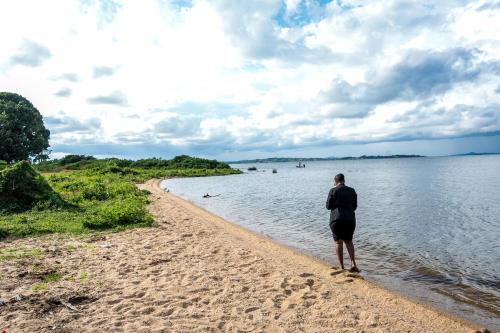 a man standing on a beach near the water at The Greige 3 Lakeside Condo in Entebbe in Entebbe