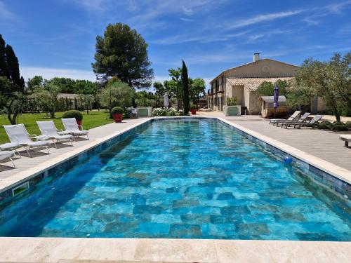 une piscine avec de l'eau bleue et des chaises blanches et une maison dans l'établissement Mas Romainho, Luxe et Charme à St Rémy, à Saint-Rémy-de-Provence